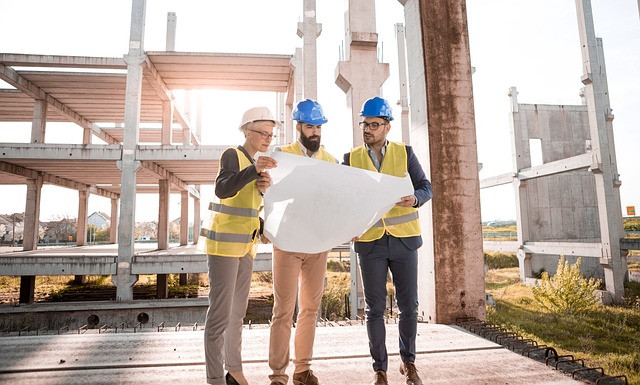Three people reading blueprints near a construction site.