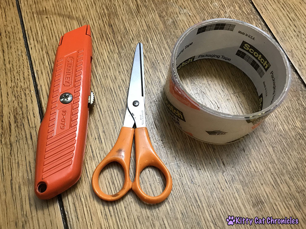 Essential supplies for building a cardboard cat castle, including boxes, box cutter, and tape.