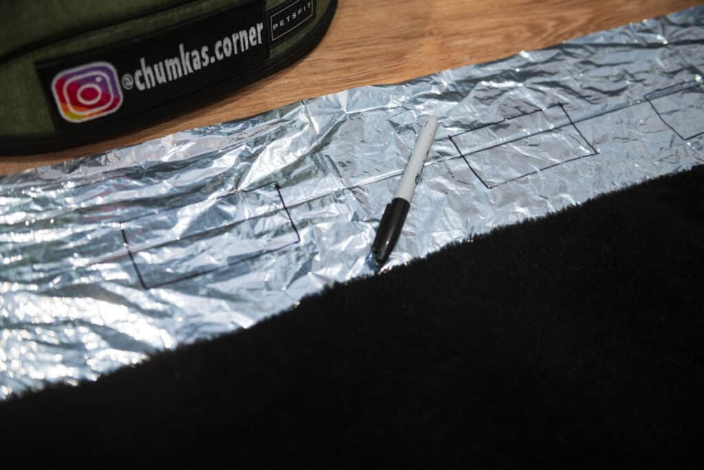 Cut out of SOL emergency blanket laying on the floor in a living room with sharpie, showing markings for velcro placement in a cat backpack carrier insulation project.