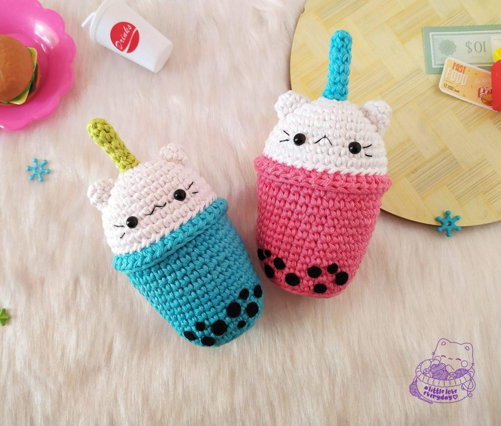 Finished boba cat amigurumi with felt boba pearls and a blue straw, sitting on a wooden surface.