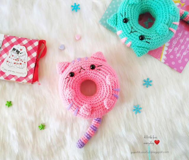 Side view of a crocheted cat donut amigurumi with purple frosting and colorful sprinkles