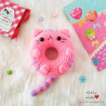 Close up of a crocheted donut cat amigurumi with pink frosting and sprinkles