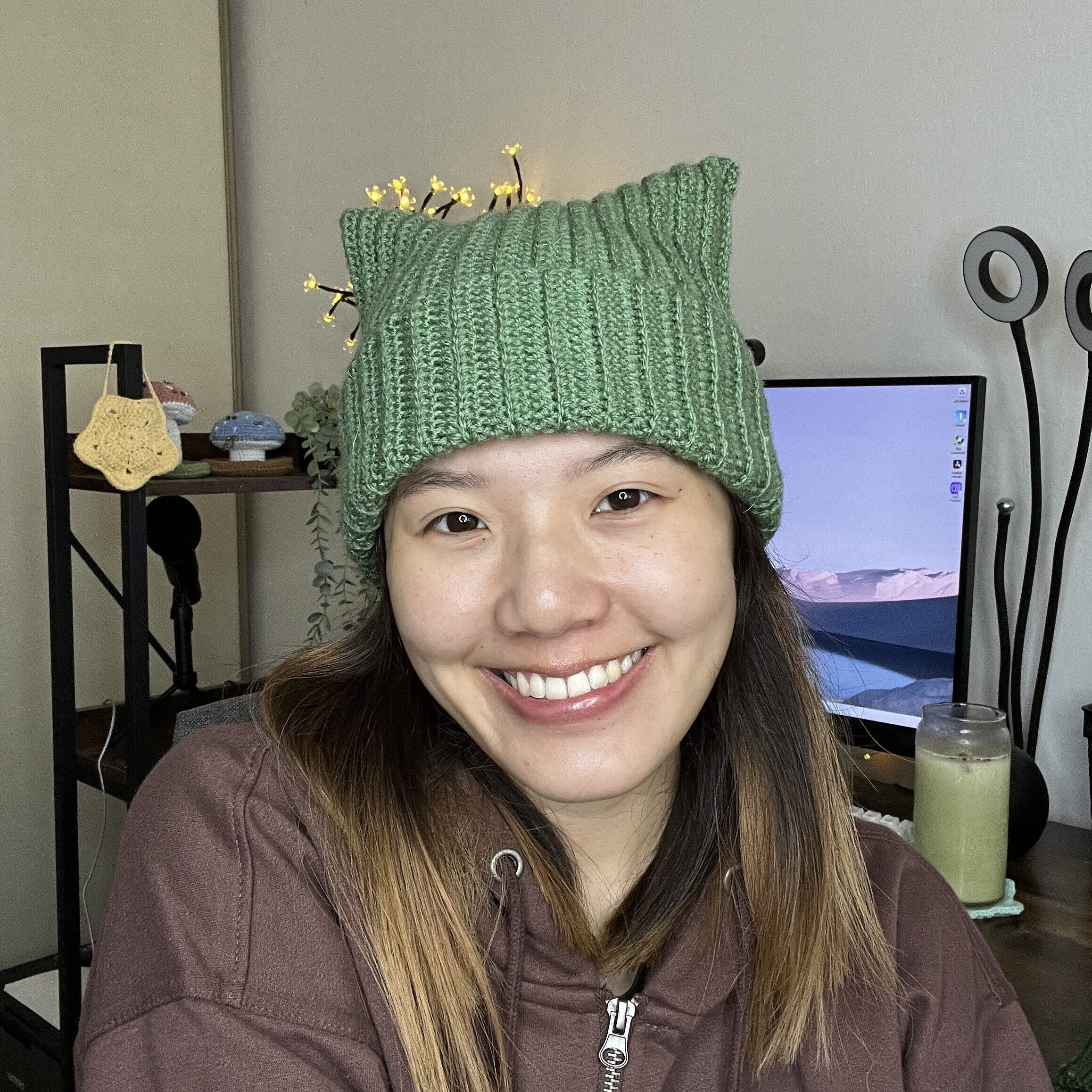 A person wearing a cream colored crochet cat ear beanie, smiling and looking to the side, with a slightly blurred background