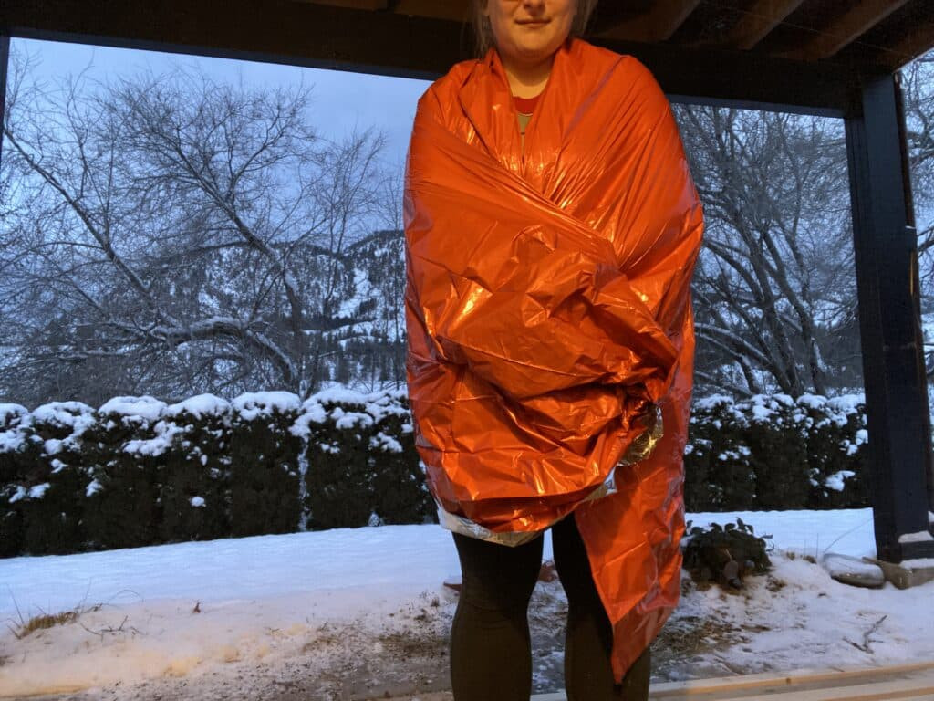 Lady standing outside in the cold winter weather. She is wrapped in emergency blanket, demonstrating its effectiveness against wind and cold for insulating a cat backpack carrier.