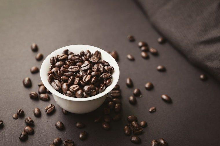 white bowl filled with coffee beans and coffee beans scattered