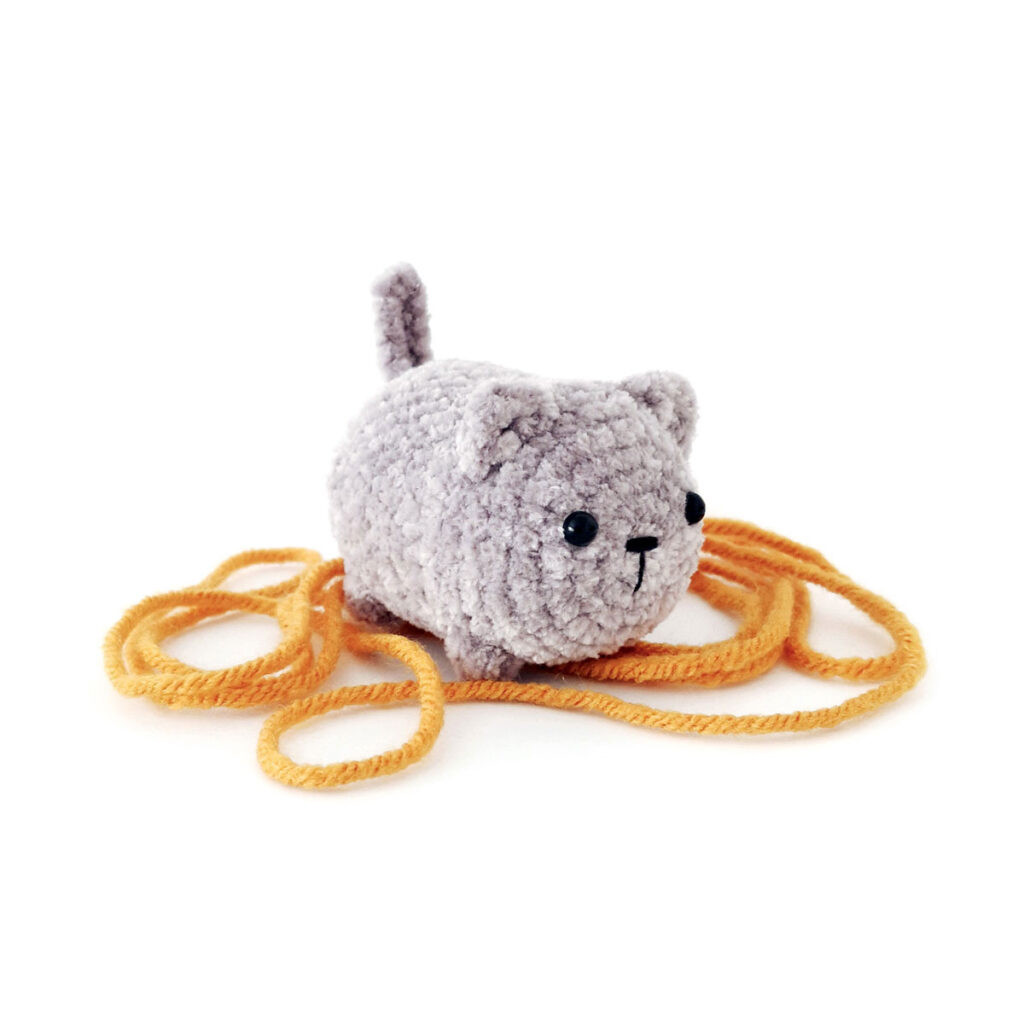 Grey crochet cat sitting on some yarn.