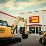 Two men in vests and hard hats stand outside The CAT Rental Store looking at CAT equipment