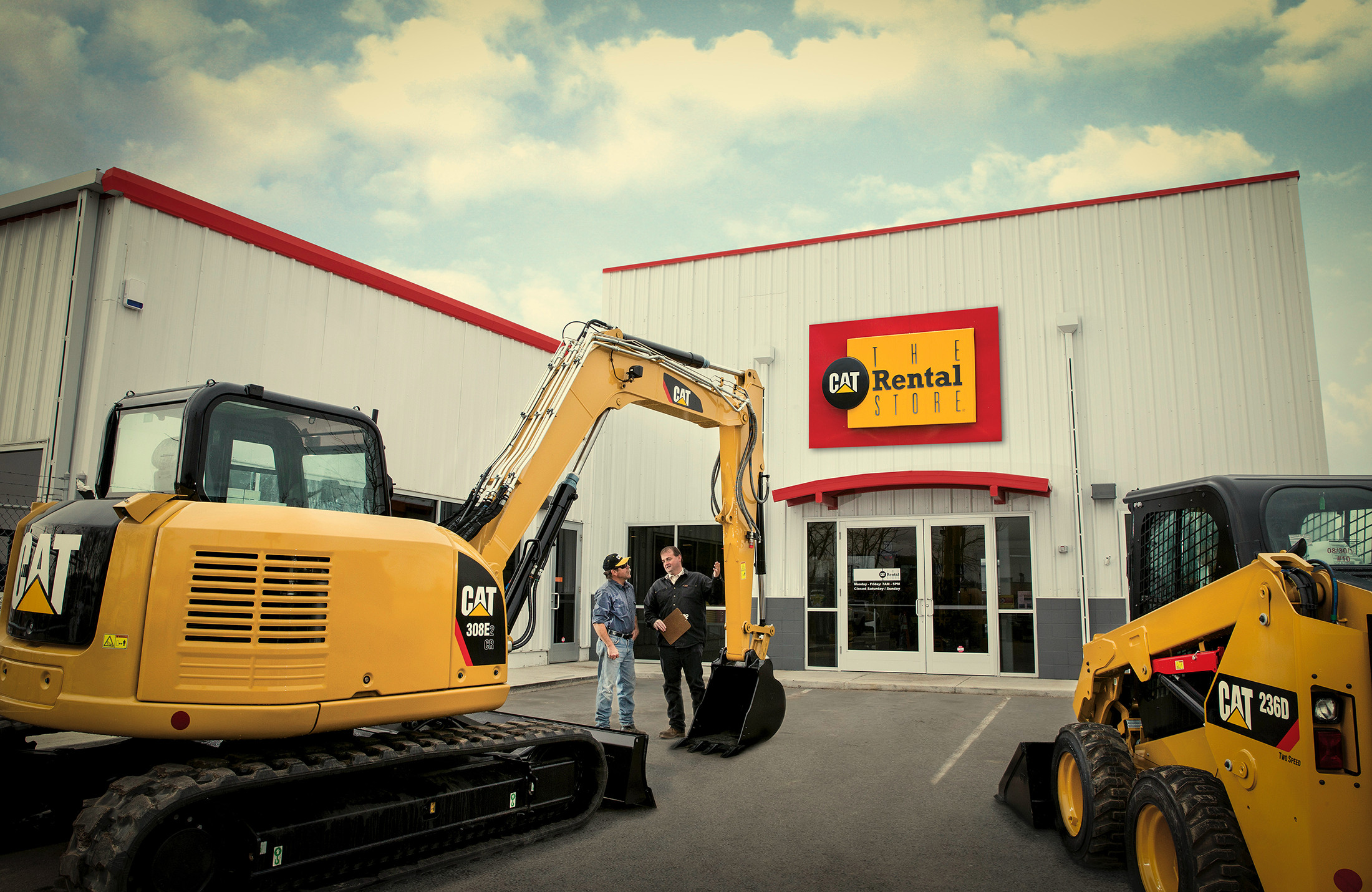 Two men in vests and hard hats stand outside The CAT Rental Store looking at CAT equipment