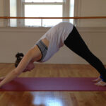 Stacey Allaire demonstrating downward dog yoga pose. Person in downward dog pose on yoga mat.