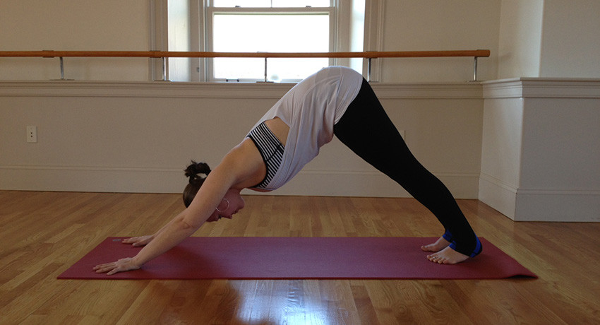 Stacey Allaire demonstrating downward dog yoga pose. Person in downward dog pose on yoga mat.